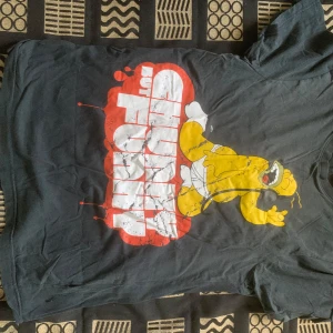 Svart Simpsons t-shirt - Cool svart t-shirt med stort tryck av Homer Simpson i gult och vitt, med texten 'Chunky but Funky' i rött och vitt. Rund hals och korta ärmar, tillverkad i mjuk bomull. Perfekt för dig som gillar roliga och unika motiv.