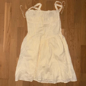 Ljus kort klänning med snörning Gina Tricot - Supersöt ljus kort klänning från Gina Tricot med broderade blommor och snörning framtill. Klänningen har axelband som knyts och är tillverkad i mjuk bomull. Perfekt för sommarens alla tillfällen, med en feminin och fräsch vibe.