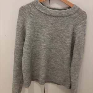Grå stickad tröja från Vero Moda - Mysig grå stickad tröja från Vero Moda i storlek XS. Tröjan har en rund halsringning och långa ärmar med ribbade muddar vid hals, ärmslut och nederkant. Perfekt för dig som gillar enkel och stilren look under kyliga dagar.