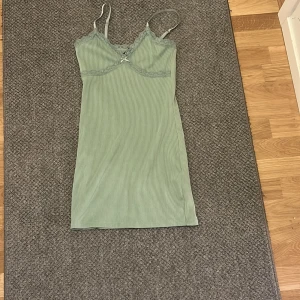 Ljusgrön ribbad klänning H&M Divided - Supersöt ljusgrön ribbad klänning från H&M Divided i storlek S. Klänningen har spetsdetaljer vid bysten, smala axelband och en liten rosett framtill. Den är figurnära och har en kort längd, perfekt för dig som gillar en enkel men ändå gullig stil.