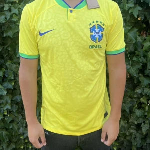 Brasilien Nike fotbollströja gul - Säljer en officiell Brasilien fotbollströja från Nike i klar gul färg med gröna och blå detaljer vid krage och ärmslut. Tröjan har korta ärmar och ett subtilt leopardmönster över hela tyget. Materialet är lätt och andas, perfekt för match eller träning.                                                                                                                                               Nypris:800kr GORILLAPRICE:499kr																						SKICK:10/10 med tagg kvar          KVITTO MEDKOMMER