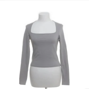 Grå långärmad topp från H&M - Snygg grå långärmad topp från H&M med fyrkantig urringning. Tillverkad i mjuk bomull med lite stretch för en bekväm passform. Perfekt att styla med jeans eller kjol för en clean look.