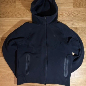 Svart hoodie från Nike, Discussable Price - Säljer en stilren svart hoodie från Nike med dragkedja och huva. Perfekt för en sportig look eller avslappnade dagar. Den har två praktiska fickor med dragkedja framtill.