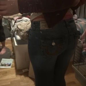 Blå jeans från True Religion - Säljer ett par snygga blå jeans från True Religion med låg midja och flare-stil för dem är tyvärr för små De har dekorativa sömmar och knappar på bakfickorna. Perfekta för en trendig look! Använt 1 gång( pris kan diskuteras)