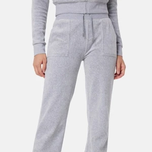 Grå Juicy Couture byxor - Snygga och bekväma grå Juicy byxor med bred resår i midjan och snörning. Byxorna har praktiska fickor fram och bak med knappdetaljer. Perfekta för en avslappnad stil.