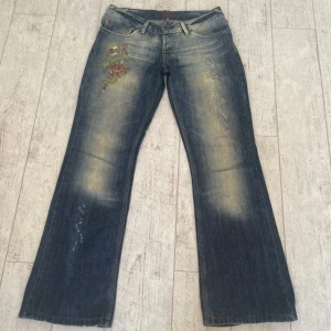 Lågmidjade bootcut jeans med detaljer - Superfina jeans som har en sliten look. Midjemått 39 cm och innerbenslängd 76cm. Står storlek L på lappen men jag skulle säga att de är storlek S-M