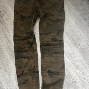 Camouflage cargopants med dragkedjor 36 - Snygga camouflage cargopants med flera dragkedjor och en cool design. Byxorna har en tight passform och är perfekta för en avslappnad stil. De har praktiska fickor och en modern look. Storlek 36 från Zara. Obehandlad fläck finns på knät
