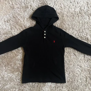 Ralph Lauren Hoodie - Tjena! En stilren svart hoodie från Ralph Lauren med röd knappslå och broderad logga på bröstet. Pris kan diskuteras!🌟