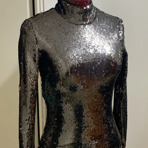 Svart glittrig paljettklänning - Snygg svart klänning täckt av glittriga paljetter som ger en fantastisk lyster. Klänningen har långa ärmar och en tight passform som framhäver figuren. Perfekt för en kväll ute eller en speciell tillställning.