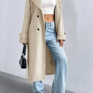 Beige trenchcoat med knappar - Snygg beige trenchcoat med knappar och bälte i midjan. Långärmad design med klassisk krage och stilrena detaljer. Perfekt för höst och vår.