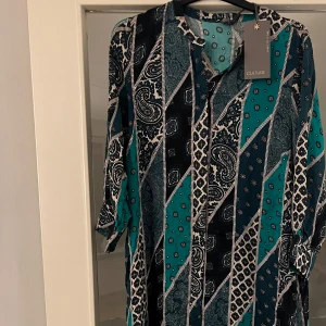 Mönstrad klänning från Culture - Snygg mönstrad klänning från Culture. Klänningen har trekvartsärmar och ett unikt paisley- och geometriskt mönster. Perfekt för en bohemisk look! Kommer med tillhörande skärp. Nypris 979kr.
