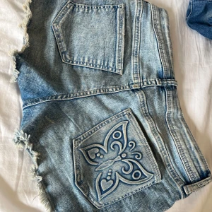 Jeansshorts med fjärilsbroderi - Snygga jeansshorts med fransiga kanter och ett coolt fjärilsbroderi på bakfickan. Perfekta för sommardagar och festivaler. De har en klassisk femficksdesign och knappgylf.