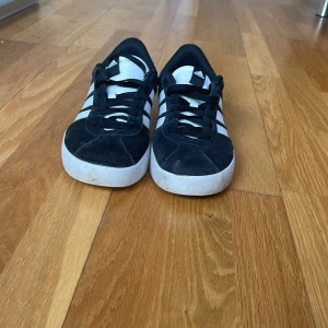 Svarta och vita sneakers från Adidas - Snygga svarta sneakers med vita detaljer från Adidas. Skorna har klassiska tre ränder på sidan och en vit sula. Perfekta för en avslappnad stil. Pris går att diskutera.