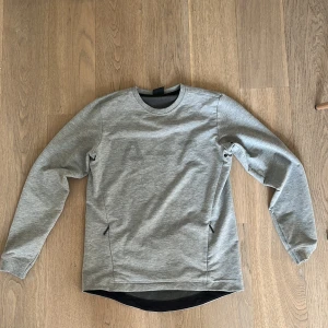 Grå tröja från A-Z - Säljer en stilren grå tröja från A-Z med diskret tryck på framsidan. Tröjan har långa ärmar och en rund halsringning. Även två diskreta fickor på framsidan.Perfekt för en avslappnad stil.