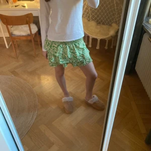 Grön blommig kortkjol - Söt grön kortkjol med blommigt mönster och volangdetaljer. Perfekt för en somrig look. Kjolen har en bekväm passform och är lätt att matcha med olika toppar.