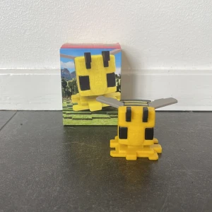 Minecraft bee - Säljer en söt Minecraft Bee figur i gult med svarta detaljer och silverfärgade vingar. Perfekt för samlare eller som dekoration för Minecraft-fans. Kommer i en färgglad förpackning med spelmotiv.