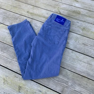Byxor från Jacob Cohen - Säljer ett par snygga blå jeans från Jacob Cohen. De har en klassisk femficksdesign och knappar i gylfen. Tillverkade av noggrant utvalda japanska tyger med italienskt hantverk. Perfekta för dig som vill ha stil och kvalitet.
