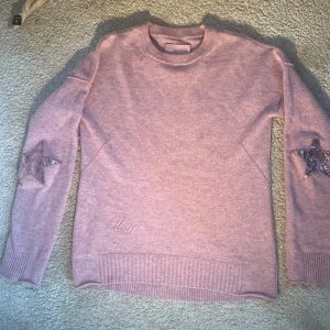 Rosa stickad tröja från Zadig & Voltaire - Säljer en snygg rosa stickad tröja från Zadig & Voltaire med stjärndetaljer på ärmarna och ett diskret ZV-märke.  Köpt i New York för 258 $ och endast använd en gång. Färgen är rosa/lila.