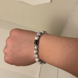 Vitt armband med marmorerade pärlor - Snyggt armband med vita marmorerade pärlor och en metallisk detalj. Perfekt för att ge en stilren touch till din outfit. Elastiskt band för enkel passform.