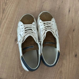 Vita och bruna sneakers från Philippe Model - Snygga sneakers från Philippe Model i vitt och brunt med snörning. Skorna har en rund tå och en kontrasterande mörkblå häl. Perfekta för en avslappnad stil.