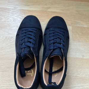 Svarta sneakers från Christian Louboutin - Snygga svarta sneakers från Christian Louboutin med den ikoniska röda sulan. Skorna har snörning och en rund tå, vilket ger en klassisk och stilren look. Perfekta för att ge din outfit en lyxig touch. Storlek 44 och 43 finns