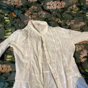Vit blus från H&M - Säljer en stilren vit blus från H&M med knappar framtill och fina spetsdetaljer. Blusen har långa ärmar och en klassisk krage. Perfekt för en elegant look.🥥⚪️🤍