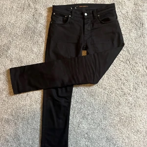 Svarta jeans från Nudie Jeans - Snygga svarta jeans från Nudie. De har en slim passform och är använda i endast ett par månader. En liten tråd som har lossnat på vänster ben men verkligen inget man tänker på, syns knappt. Hör av dig vid minsta fundering