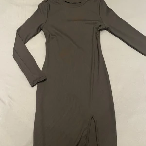 Svart ribbad klänning med slits  - Snygg svart ribbad klänning med lång ärm och en liten slits framtill. Perfekt för en stilren look. Klänningen har en tight passform som framhäver figuren.