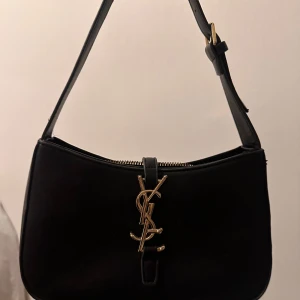 Svart väska, ysl (inte äkta) - Elegant svart väska ysl. Väskan har en dragkedja och ett justerbart axelband. Perfekt för att ge en lyxig touch till din outfit.