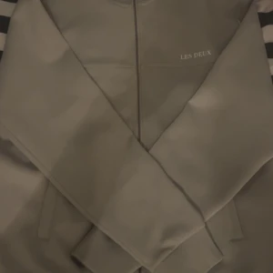 Beige zip-hoodie från Les Deux - Snygg grå jacka från Les Deux med dragkedja framtill. Perfekt för en stilren look. Jackan har långa ärmar och en minimalistisk design. En liten defekt på höger ben inte så märkvärdigt 