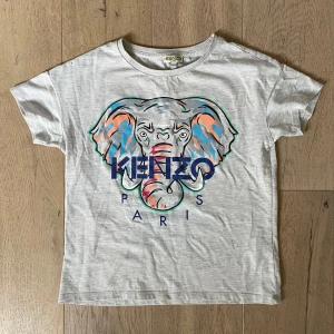 Grå t-shirt med elefantmotiv från Kenzo - Säljer en cool grå t-shirt från Kenzo med ett färgglatt elefantmotiv och texten 'Kenzo Paris' på framsidan. Perfekt för en stilren och trendig look. Passar bra till både jeans och shorts!