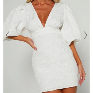 Vit klänning med puffärmar - Elegant vit klänning med djup v-ringning och puffiga trekvartsärmar. Klänningen har en åtsittande passform och är dekorerad med ett subtilt blommönster. Perfekt för sommarens festligheter. Sitter för stort på mig och för sent att lämna tillbaka den så därav säljer jag! Köpte för 900kr, den är helt oanvänd. Den är i storlek 40 men den sitter mer som en 38!