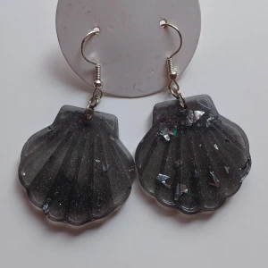 Svarta snäckformade örhängen - Dessa är 2a utrensning! Snygga svarta örhängen i form av snäckor med en glittrig yta. Perfekta för att ge en unik touch till din outfit. De hänger från en enkel krok och har en skimrande effekt som fångar ljuset.