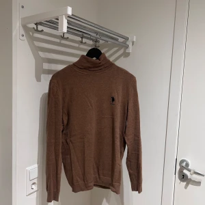 Brun polotröja från Ralph Lauren - Säljer en stilren brun polotröja från Ralph Lauren med en diskret logga på bröstet. Tröjan har långa ärmar och är perfekt för kyligare dagar. Passar både till vardags och mer uppklädda tillfällen stl m men kan passa s.