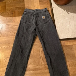 Svarta jeansbyxor från Carhartt - Snygga svarta jeansbyxor från Carhartt med klassisk femficksdesign. Byxorna har en rak passform och är tillverkade i slitstarkt material. Perfekta för en avslappnad stiloch en kylig vår och sommar kväll