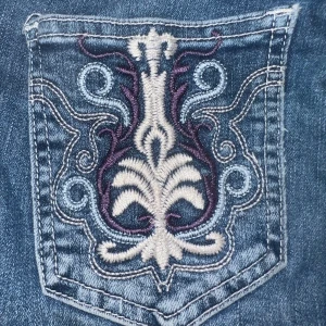 Bootcut jeans med broderade bakfickor - Snygga blå jeans med unika broderade detaljer på bakfickorna. Knappt använda och när jag köpte dem så stog det lågmidjade men de är mid waist. Super finna annars och  jenasen har en klassisk femficksdesign och en knappgylf. Använda men i fint skick. Ändå är nött mellan benen (se bild), ett litet hål där men det ska vara lätt att laga. Inköpta för 450kr säljer för 299kr