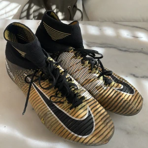 Nike Mercurial fotbollsskor i guld och svart - Säljer ett par Nike Mercurial fotbollsskor i en cool kombination av guld och svart. Skorna har snörning och en rund tådesign. Perfekta för fotbollsplanen med sin snygga look och funktionalitet. Sällsynta CR7 skor
