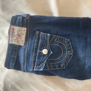 Blå jeans från True Religion - Snygga blå jeans från True Religion med ikoniska bakfickor och kontrastsömmar. Klassisk femficksdesign med knappgylf och bälteshällor. Skriv om ni har frågor🥰