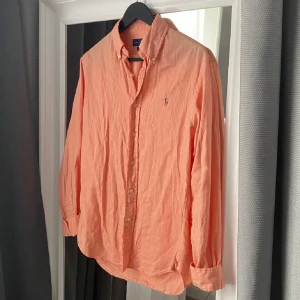 Persikofärgad skjorta från Ralph Lauren - Snygg orange skjorta från Ralph Lauren. Skjortan är väl använd men har tagits väl hand om. Passar perfekt nu till vår/sommar. Storlek på skjortan är S. Nypris ca 1400 kr, mitt pris 300 kr! Hör av er vid fler frågor och funderingar!