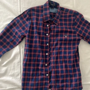 Rutig skjorta från GANT - Snygg rutig skjorta från GANT i blått och rött. Skjortan har långa ärmar och knappar framtill. Perfekt för en stilren look med en casual fit. Broderad logga på bröstet ger en extra touch.