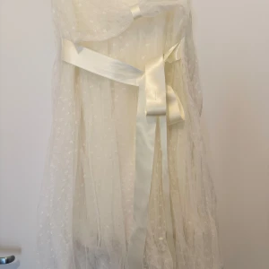 Vit glitter-prickig klänning från Ida Sjöstedt - Elegant vit klänning från Ida Sjöstedt med prickigt mönster och vackra satinband. Klänningen har en luftig design med ett skirt tyg som ger en romantisk känsla. Perfekt för speciella tillfällen.