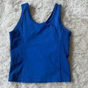 Blå träning linnetopp från Röhnisch st.170 - Säljer en snygg blå linnetopp från Röhnisch. Perfekt för träning eller en varm sommardag. Toppen har en enkel design med breda axelband och är tillverkad i ett mjukt och stretchigt material.