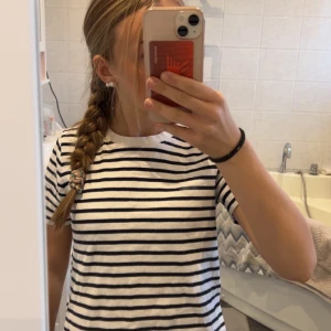 Randig t-shirt från Zara - Säljer en klassisk randig t-shirt från Zara i svart och vit. Perfekt för en avslappnad stil. T-shirten har korta ärmar och en rund halsringning.