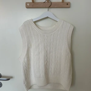 Vit stickad väst från Lindex - Säljer en stilren vit stickad väst från Lindex. Den har ett klassiskt flätmönster och ribbade kanter. Aldrig använd ❤️