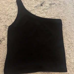 Svart one shoulder topp från Gina Tricot - Snygg svart one shoulder topp från Gina Tricot. Perfekt för en stilren look med en asymmetrisk design. Passar utmärkt till både jeans och kjol.