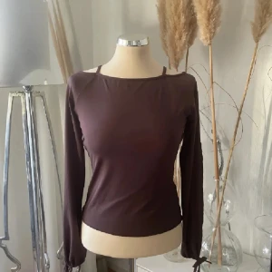 Brun långärmad topp - Säljer en stilren brun långärmad topp med en enkel design. Perfekt för en minimalistisk look. Toppen har en rund hals och är tillverkad i ett mjukt material. Med sprung i ärmarna 