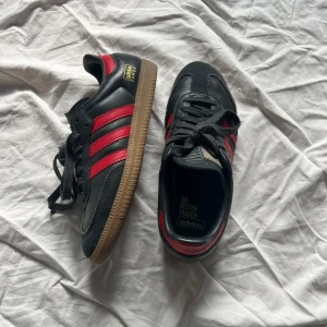 Svarta och röda Adidas Samba - Snygga Adidas Samba i svart med röda detaljer och klassiska tre ränder. Skorna har en gummisula och snörning. storlek 36,5 knappt använda!