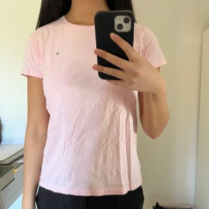 Ljusrosa t-shirt från Gant - Säljer en ljusrosa t-shirt från Gant med en liten logga på bröstet. T-shirten har en klassisk rund hals och korta ärmar. Fint skick. Passar någon som är xs/s även om den är köpt i ”170 cm, 15 years”