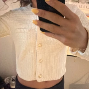 Beige cardigan - Superfin beige cardigan med snygg struktur och dekorativa guldknappar framtill. Modellen är croppad med lång ärm och har två fickor på bröstet. Perfekt för dig som vill ha en stilren och trendig look till vardags.❤️använd 1 gång (när bilden togs)