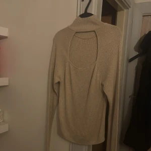 Glittrig beige polotröja med öppen framsida  - Supersnygg beige polotröja med glittrigt tyg och lång ärm. Tröjan har en cool öppen framsida som gör den extra unik. Perfekt för dig som vill sticka ut lite extra med en trendig och stilren look. Exempelvis bra till ute kvällar eller fester osv 